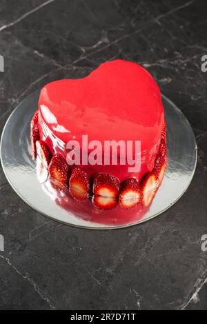 Beautiful heart-shaped moist mud cake with a ganache coating, red mirror glaze, and a fresh strawberry border. Stock Photo