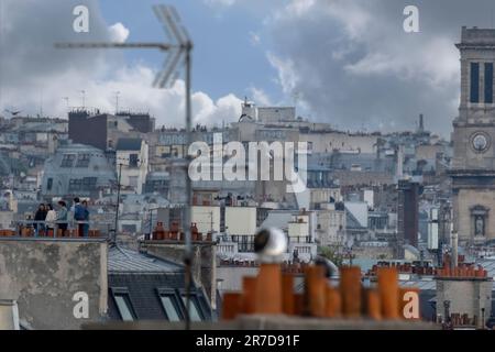 Selective focus aerial view of rooftops in Paris showing clay chimney pots, gothic tower, TV antenaes and people on a rooftop terrace Stock Photo