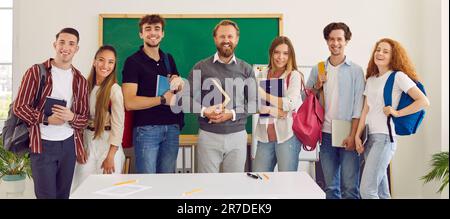 Photo of classmates and teacher standing against green chalk board on background. Stock Photo