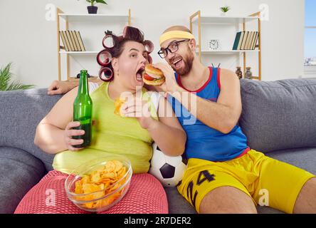 Funny man and fat woman having cheat day, sitting on sofa and eating unhealthy food Stock Photo