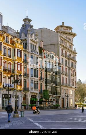 Oviedo, Spain - February 12, 2023: Pedestrians walk along a city street with street lights. A modern commercial building dominates the downtown landsc Stock Photo