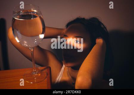 A young woman posing next to a glass of water near a window. Stock Photo