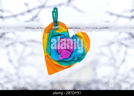 Multicolored paper heart on a clothespin. Heart from crumpled paper on a snowy background. Stock Photo