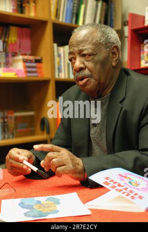 A young man sitting at a desk, looking at a smartphone while reading Stock Photo