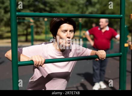 Mature woman doing push-ups from the crossbar on outdoor sports ground Stock Photo