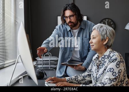 Side view portrait of senior woman using computer in class with male teacher helping, copy space Stock Photo