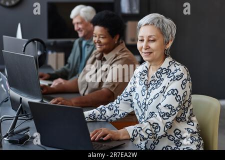 Side view portrait of senior Asian woman using computer in programming class for seniors Stock Photo