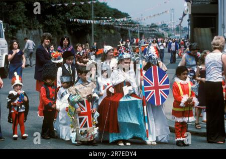 Queen Elizabeth II Silver Jubilee celebration 1977.  Neighbourhood street party in Podmore Street, outside the Royal Standard public house. Children in fancy dress, a girl is the Queen of the street wearing a silver paper crown and hooped skirt, while an other child carries a Union Jack shield and three spiked spear lance. Wandsworth south London, England circa June 1977. Stock Photo