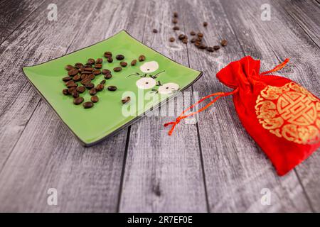 Coffee beans on a green saucer with a red pouch next to it, wooden background, photo at an angle Stock Photo