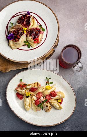 A vertical image of two white plates of pancakes, both filled with different toppings such as blueberries, raspberries, and syrup Stock Photo