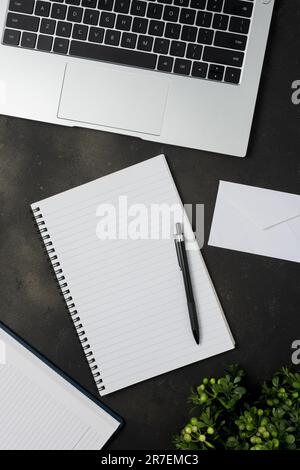 Black office desk table with blank notebook, laptop and other office supplies. Top view with copy space. Stock Photo