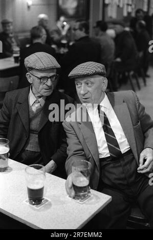Byker and St Peters Working Men's Club, Newcastle upon Tyne, Tyne and Wear,  northern England 1973.  Saturday night and two smartly dressed men friends chat together over a pint of beer, both men are wearing flat tweed cloth caps, typical of the period. 1970S UK HOMER SYKES Stock Photo