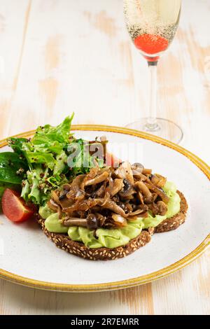 Open sandwich with mushrooms, guacamole avocado and greens on wooden backround. Healthy breakfast. Stock Photo