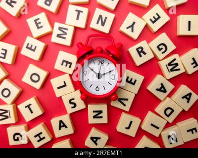 A close-up of a red alarm clock surrounded by a collage of colorful blocks with different letters on a pink background Stock Photo
