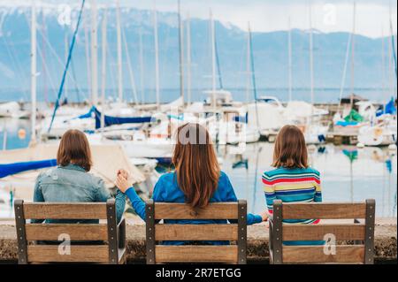 Outdoor portrait of happy mother and two young teenage girls resting by the lake. Image taken in Lausanne, Switzerland. Back view Stock Photo