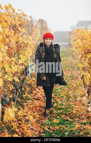 Young woman hiking in Lavaux vineyards in autumn, wearing warm military jacket and red beret Stock Photo