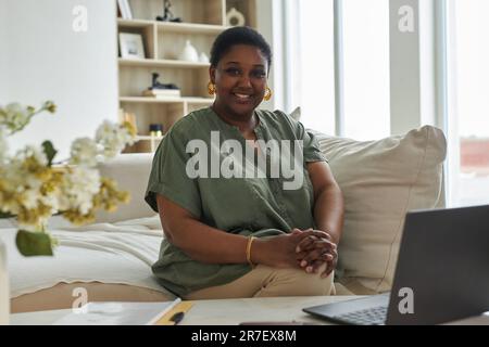 Portrait of African American woman smiling at camera while working on laptop at home Stock Photo