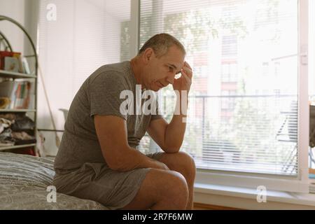 Middle-aged man in bedroom sitting on bed Stock Photo