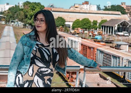 A Caucasian young woman dressed in a long flowing gown stands on the bridge in the urban city Stock Photo