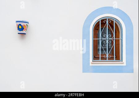 A Wooden window with bars with blue rims and decorative plant pot on the wall Stock Photo