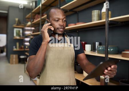 African pottery studio manager using a phone and tablet in a workshop Stock Photo