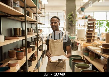 Smiling African potter doing inventory of pots on shelves in a ceramics studio Stock Photo