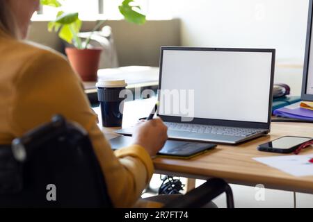 Caucasian casual businesswoman in wheelchair using graphics tablet and laptop, copy space on screen Stock Photo