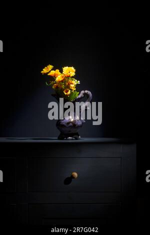 still life of a yellow flower in a vase on a sideboard. Blue background Stock Photo