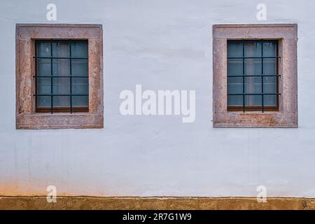 An exterior shot of a building featuring two windows with tan trim against a white stucco wall Stock Photo
