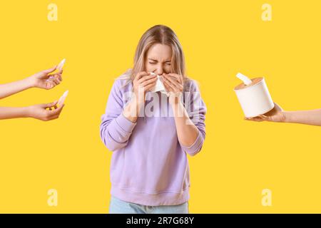 Allergic young woman and female hands holding drops and tissue box on yellow background Stock Photo