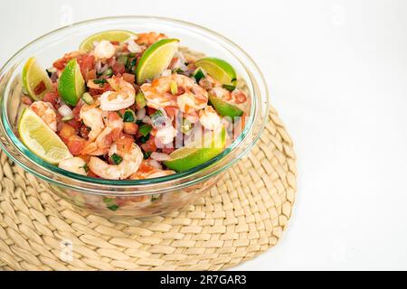 Fresh shrimp salad with lime slices in a glass bowl on a bamboo mat isolated on white Stock Photo