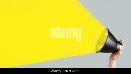 Bull horn, loud speaker, megaphone with yellow light beam in hand, banner background for announcing, promoting. Stock Photo