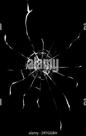 Cracks in the window from a shot from a weapon. Damaged window glass. White cracks on a black background. Stock Photo