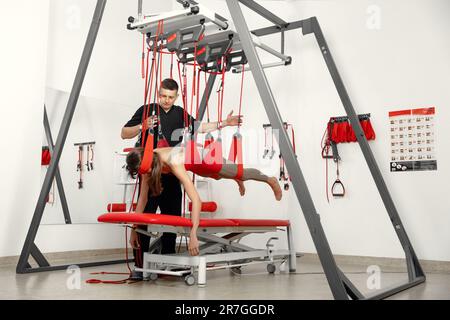 physical therapy, Physical rehabilitation, Health-improving exercises, doing exercises, decompression simulators. Rehabilitation exercises on red cord slings to restore pain-free movement patterns and enhance overall body functions Stock Photo