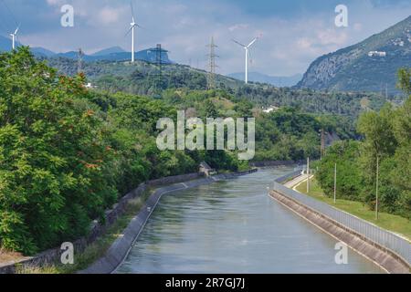 The Biffis canal, an artificial canal for irrigation and hydroelectric purposes with wind turbines in the background. Together these provide clean ene Stock Photo
