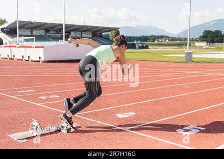 Young woman preparing for the run race, taking a start position for sprint, using starting block Stock Photo