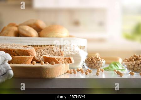 Slices and bread with soy flour on cutting board and in basket on white kitchen bench. Front view. Stock Photo