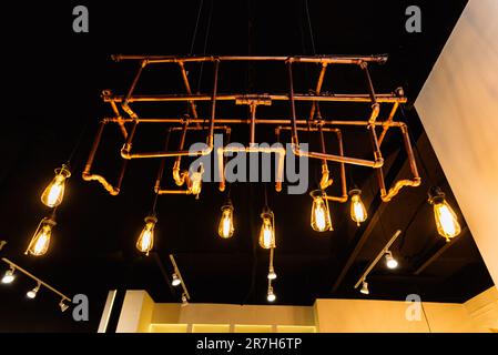 Ceiling light bulbs on copper pipes decorate the interior of the dark room. Stock Photo