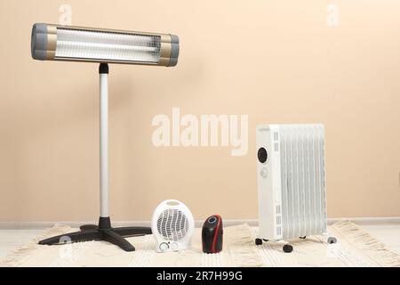 Different modern electric heaters on floor near beige wall indoors Stock Photo