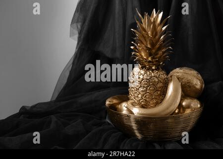 Golden bowl with fruits on black fabric against light grey background. Space for text Stock Photo