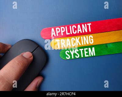Wireless mouse and wooden stick with the word APPLICANT TRACKING SYSTEM on blue background Stock Photo