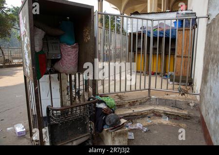 A homelss man sleeping beside an Abandoned card phone booth at Kamlapur railway station in Dhaka, Bangladesh Stock Photo