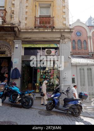 Woam in traditional muslim clothes walks down a steep quaint street in the Galata area of Istanbul, Turkey. Motorbikes are parked along the road. Stock Photo