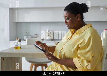 African American woman using tablet pc while sitting in the kitchen Stock Photo
