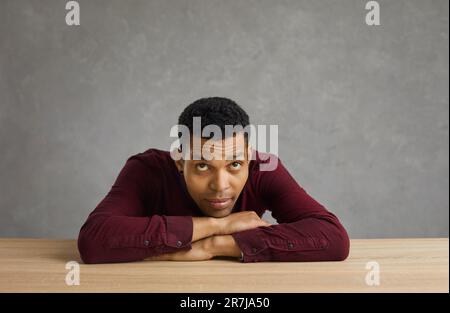 Sad thoughtful man putting head on hands sitting at desk studio portrait Stock Photo