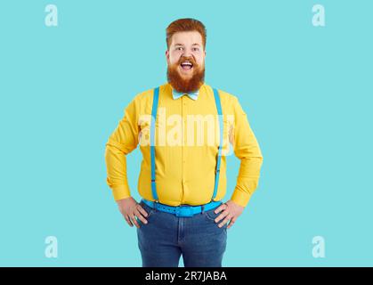 Funny big size Caucasian man with red beard looks at camera with mouth open and holds hands on belt Stock Photo