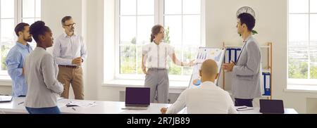 Colleagues near whiteboard with graphs in office discussing results of marketing research. Stock Photo