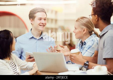 Group of cheerful young multi-ethnic students standing in circle and discussing ideas for project in library Stock Photo