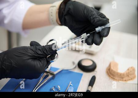 Close-up dentist's hands recharging cartridge with anesthetic in stainless steel syringe, preparing dental anesthesia Stock Photo