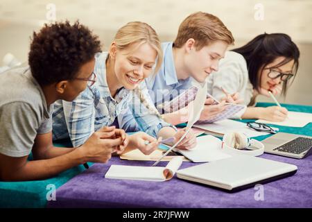 Group of positive multi-ethnic students in casual clothing lying in row on soft poufs preparing for difficult test Stock Photo
